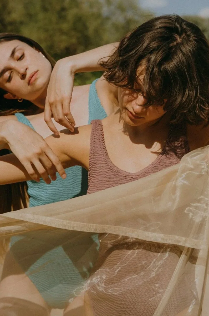 Two women in one-piece swimsuits enjoy a sunny day outdoors, embracing the summer vibe.